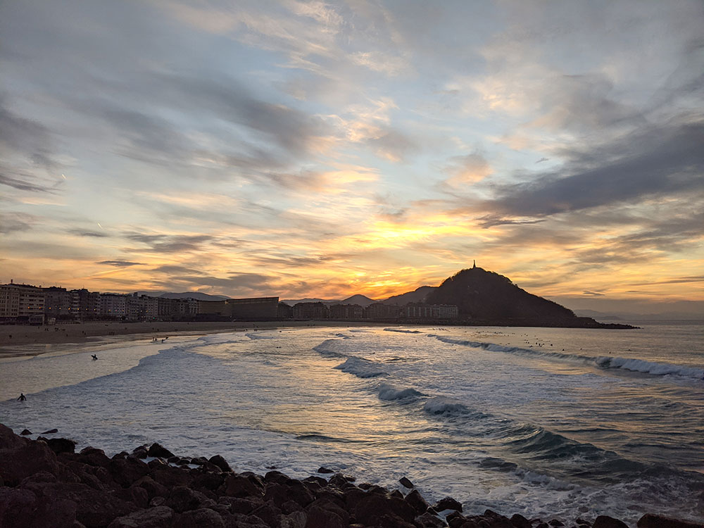 puesta de sol sobre la playa de zurriola en san sebastian con el monte urgull al fondo