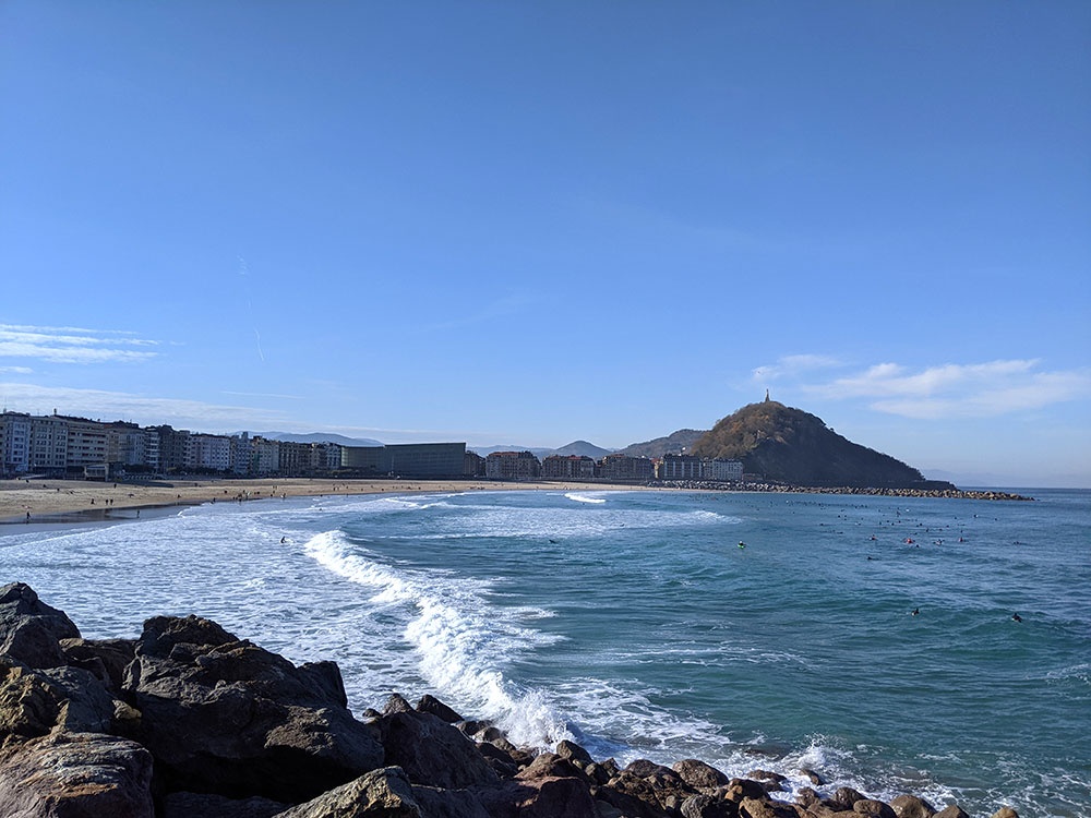 Sentado en la pared en Sagues Gros viendo a los surfistas en el mar en la playa de la Zurriola