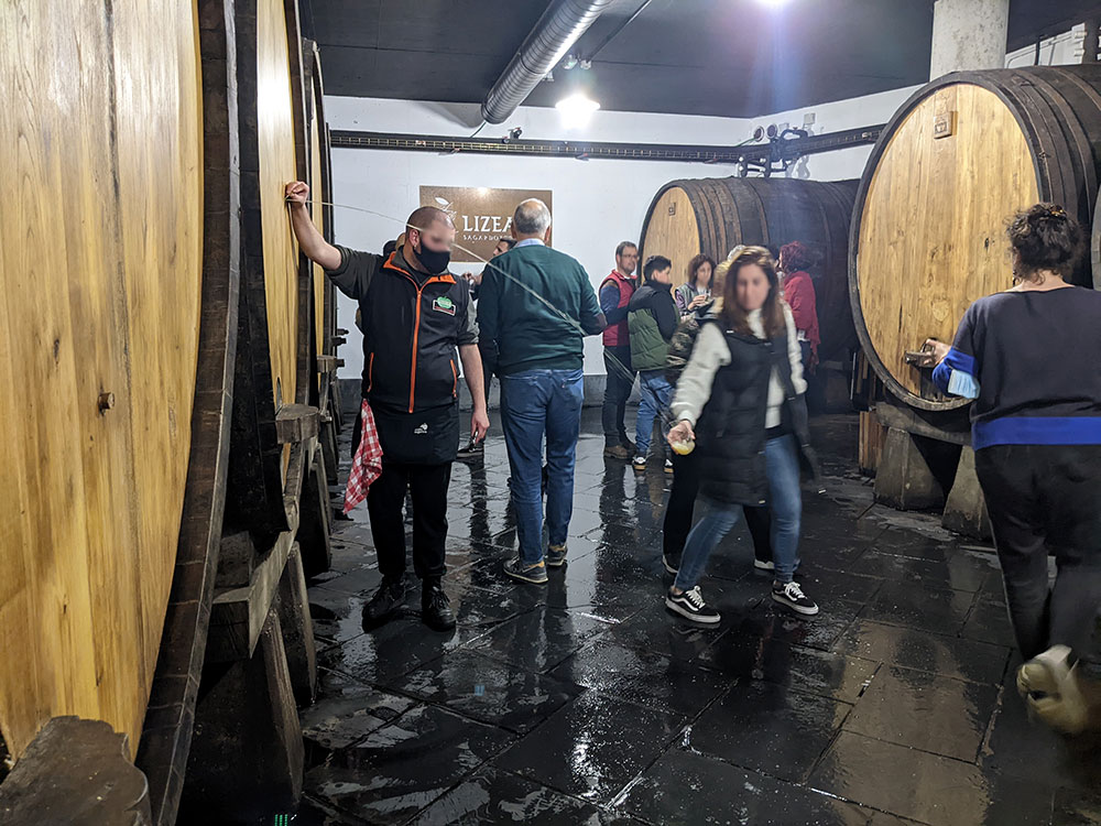Gente tomando sidra vasca de un barril de sidra en una sidrería de Astigarraga