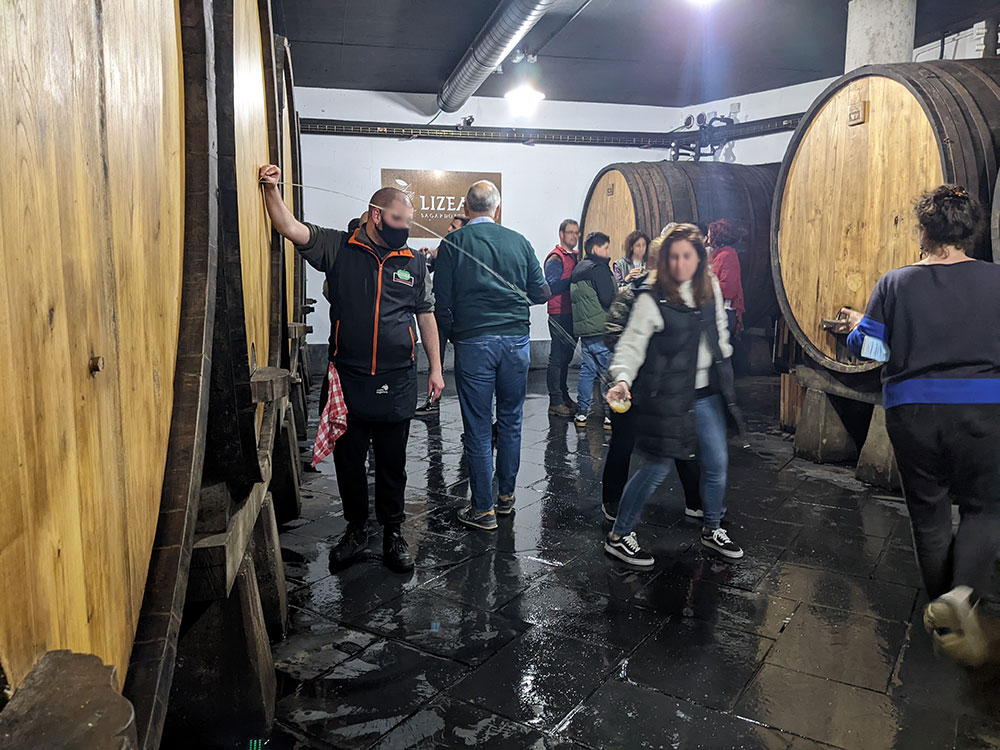 Gente tomando sidra vasca de un tonel de sidra en una sidrería de Astigarraga